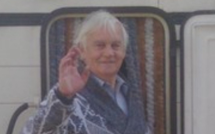 Starszy mężczyzna machający ręką, uśmiechający się do kamery.