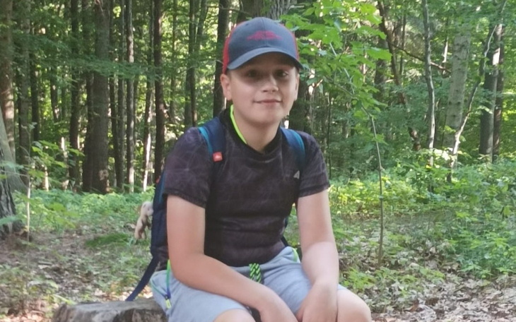 Chłopiec siedzący na pniu w lesie, otoczony zielenią.