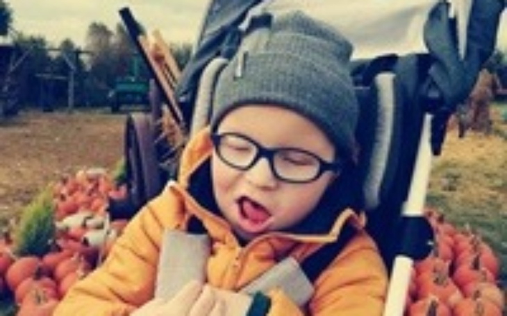 Chłopiec w ciepłej kurtce, siedzący w wózku, otoczony dyniami.