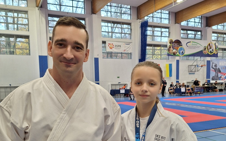 Trener z młodą zawodniczką karate na zawodach sportowych.
