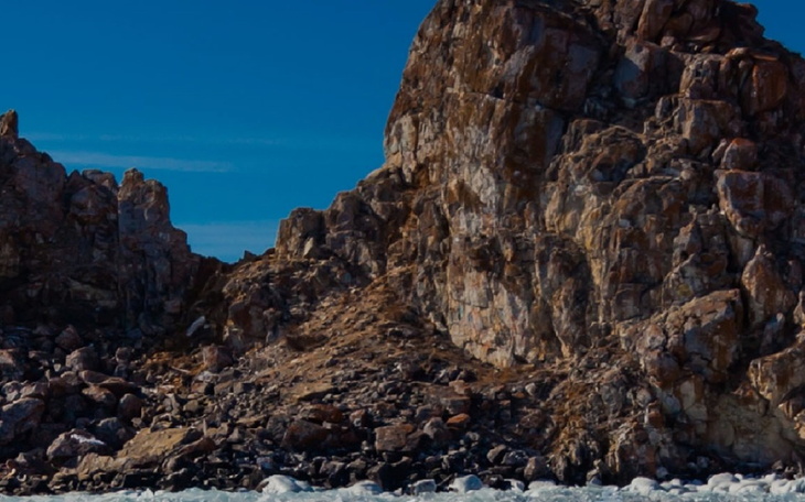 Surowe skały nad brzegiem morza, w tle błękitne niebo.