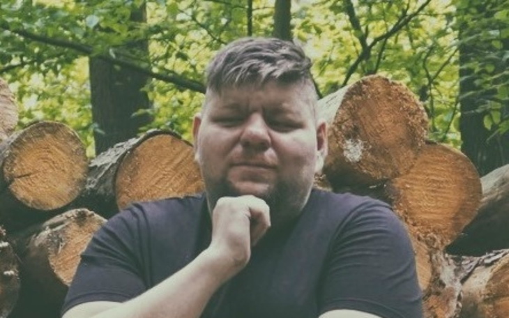 Mężczyzna w lesie, pozujący z drzewami w tle.