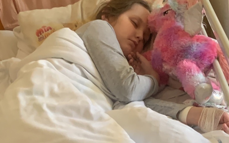 Dziewczynka śpi w łóżku z pluszowym jednorożcem.