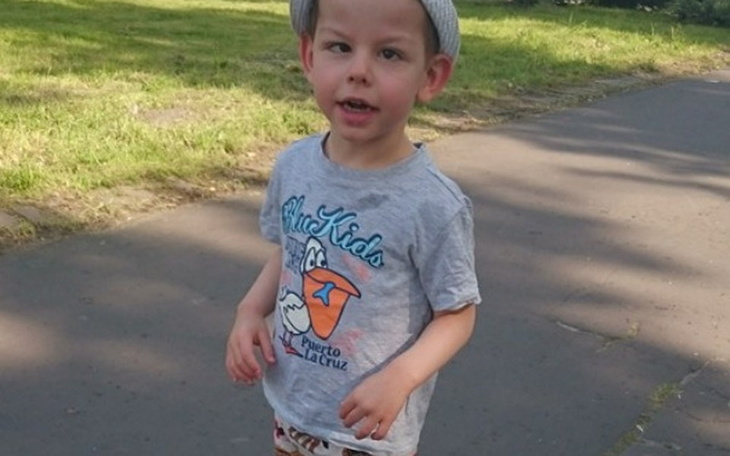 Chłopiec spacerujący po parku, uśmiechnięty i w letnim stroju.