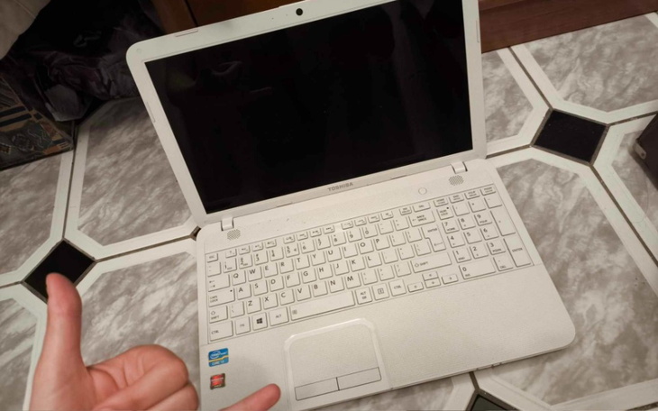 Biały laptop Toshiba na stole, z kciukiem w górę obok.