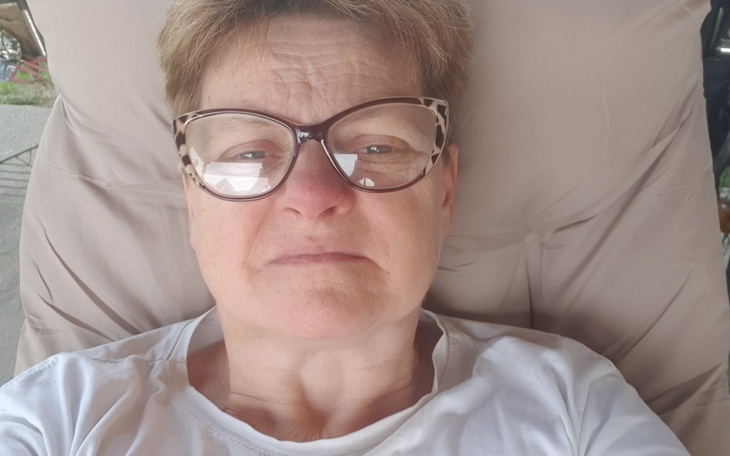 Kobieta w okularach, leżąca na leżaku i patrząca w kamerę.