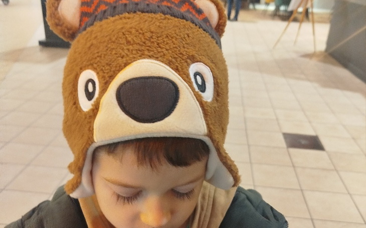 Chłopiec w czapce misia, skupiony na czymś, z uśmiechem na twarzy.