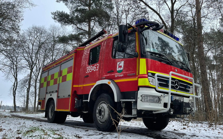 Czerwony wóz strażacki na leśnej drodze w zimowej scenerii.