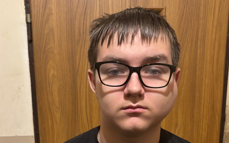 Młody mężczyzna z okularami, stojący przed drzwiami.