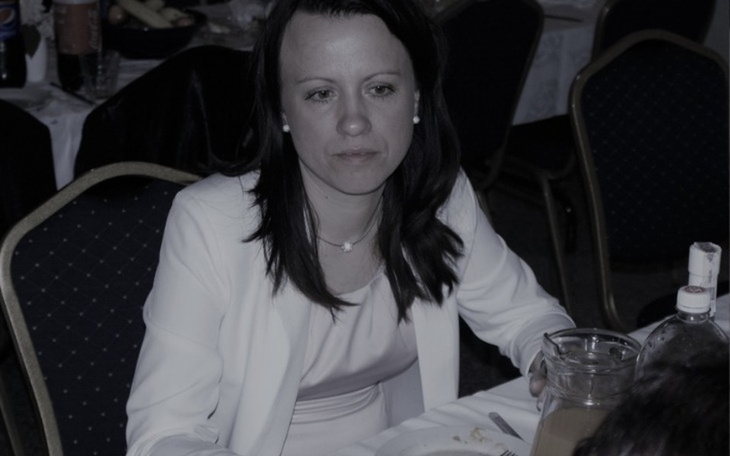 Kobieta w białej bluzce, siedząca przy stole, zamyślona.