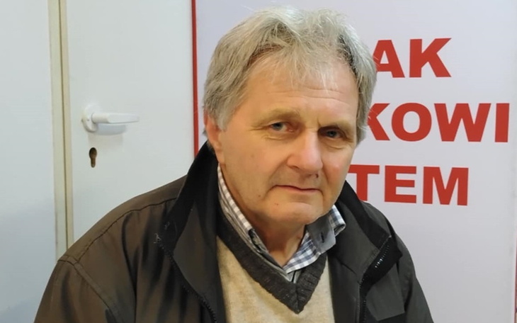 Starszy mężczyzna siedzący w pomieszczeniu, z poważnym wyrazem twarzy.