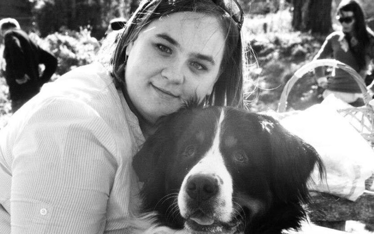 Kobieta przytulająca psa na tle zieleni.