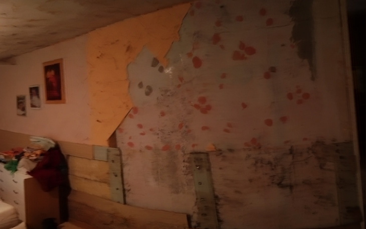 Zniszczona ściana w pomieszczeniu, z odpadami i plamami.