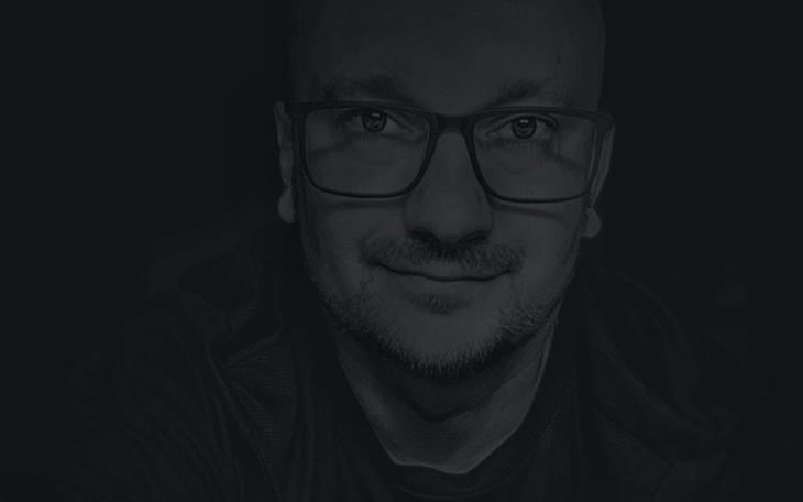 Portret mężczyzny w okularach, z uśmiechem na twarzy.