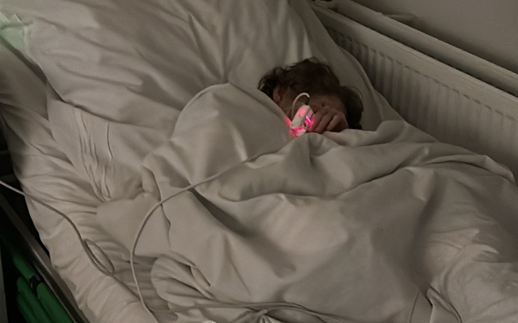 Dziecko śpiące w łóżku, przykryte kocem, z urządzeniem medycznym.