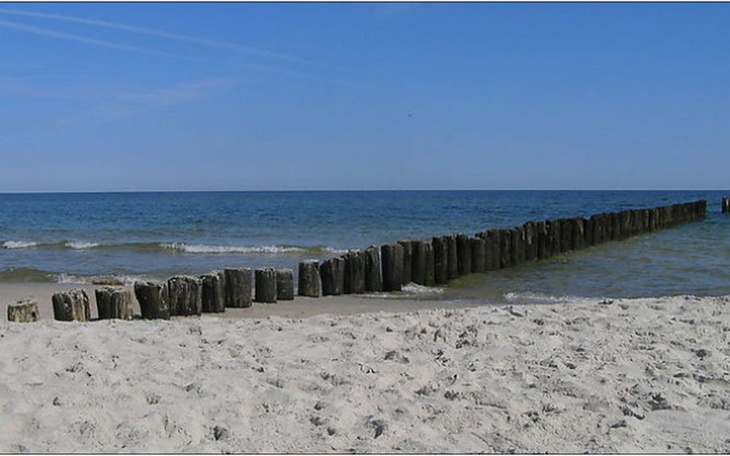 Widok na plażę z drewnianymi pomostami i spokojnym morzem.