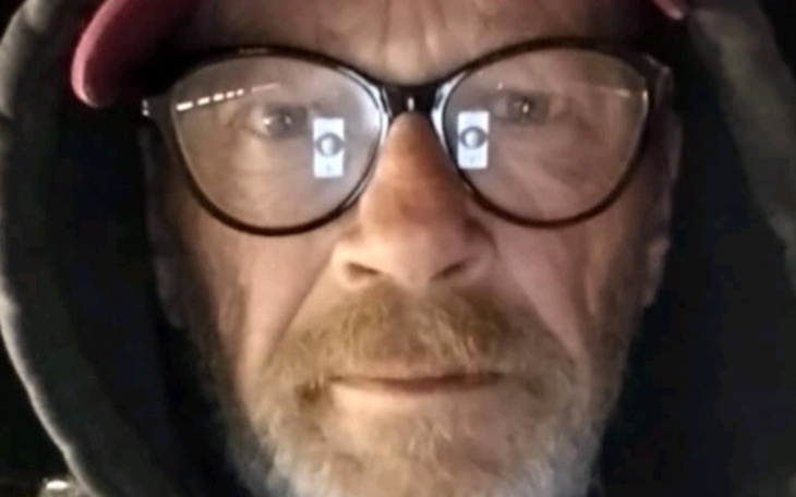 Mężczyzna w okularach, z brodą, patrzy w kamerę.