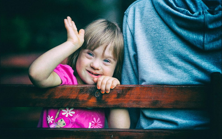 Dziewczynka z zespołem Downa machająca z uśmiechem.