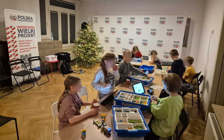 Dzieci bawiące się w sali z zabawkami, choinka w tle.