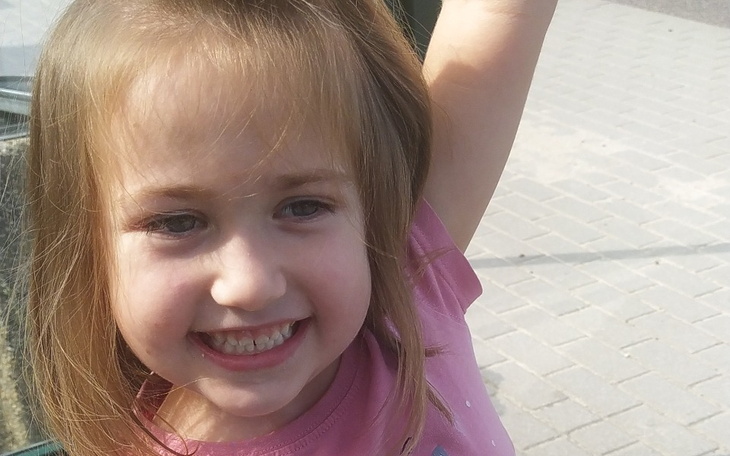 Mała dziewczynka z uśmiechem, podnosi rękę w geście radości.