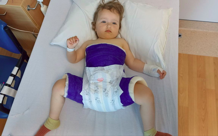 Dziecko w szpitalu, z opatrunkiem na ciele, leży na łóżku.