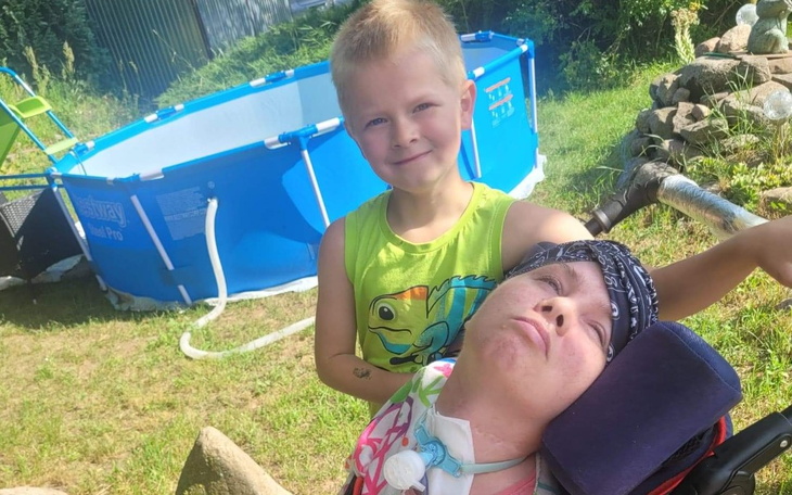 Chłopiec z uśmiechem stoi obok osoby na wózku inwalidzkim.