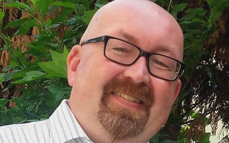 Mężczyzna uśmiechający się w otoczeniu zieleni.