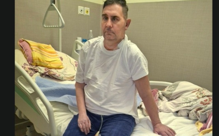 Mężczyzna siedzący na łóżku w szpitalu, wygląda na zmęczonego.