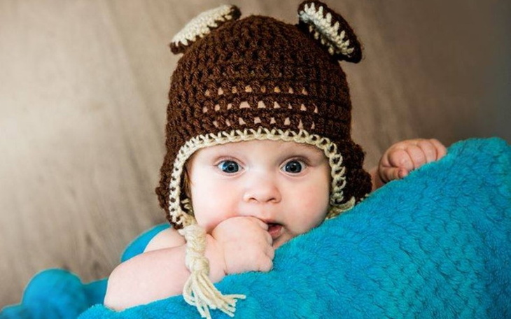 Małe dziecko w czapce misia, uśmiechające się do obiektywu.