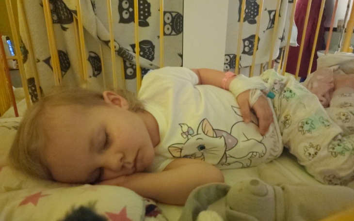 Śpiąca dziewczynka w łóżeczku, trzymająca rękę na sercu.