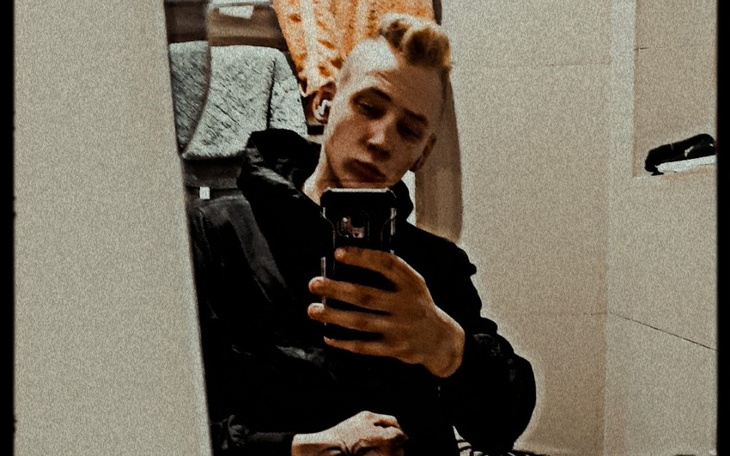 Młody mężczyzna robi selfie w lustrze w ciemnym ubraniu.