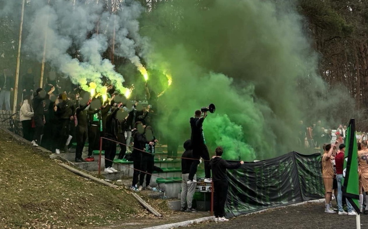 Grupa kibiców na stadionie, z dymem w powietrzu.