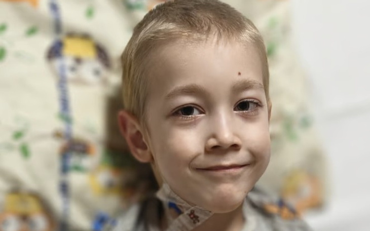 Chłopiec uśmiechający się w szpitalnym łóżku, z opatrunkiem na szyi.