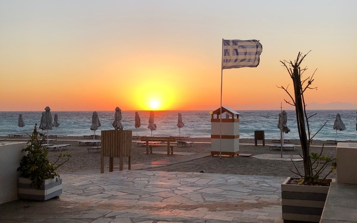 Zachód słońca na plaży z leżakami i flagą.