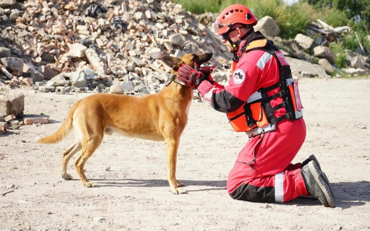 Ratownik w czerwonym stroju, przytulający psa ratunkowego.