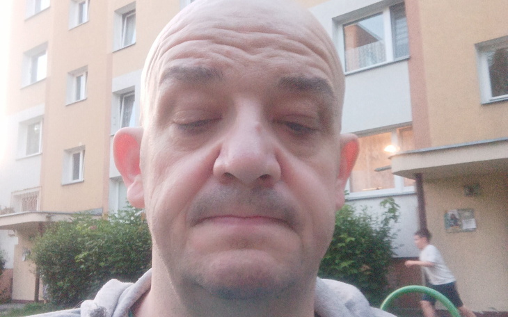 Mężczyzna z zamyśloną miną, w tle blok mieszkalny.