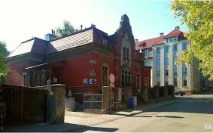 Zabytkowy budynek w mieście, otoczony zielenią.