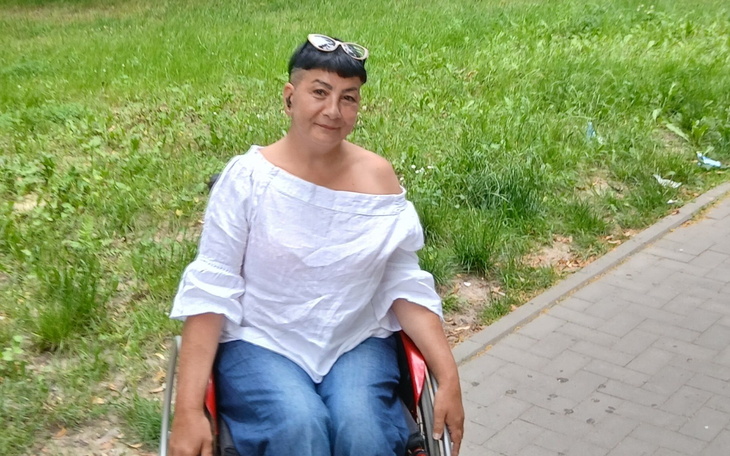Kobieta w wózku inwalidzkim na tle zielonej trawy.