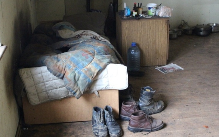 Zniszczony pokój z łóżkiem i brudnymi butami na podłodze.