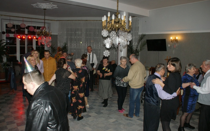 Uczestnicy zabawy tanecznej w eleganckiej sali, radosna atmosfera.