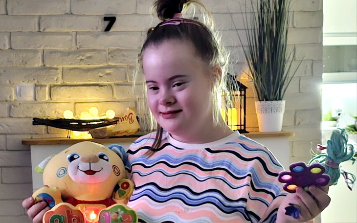 Dziewczynka z zespołem Downa trzymająca kolorowe zabawki, uśmiechająca się do kamery.