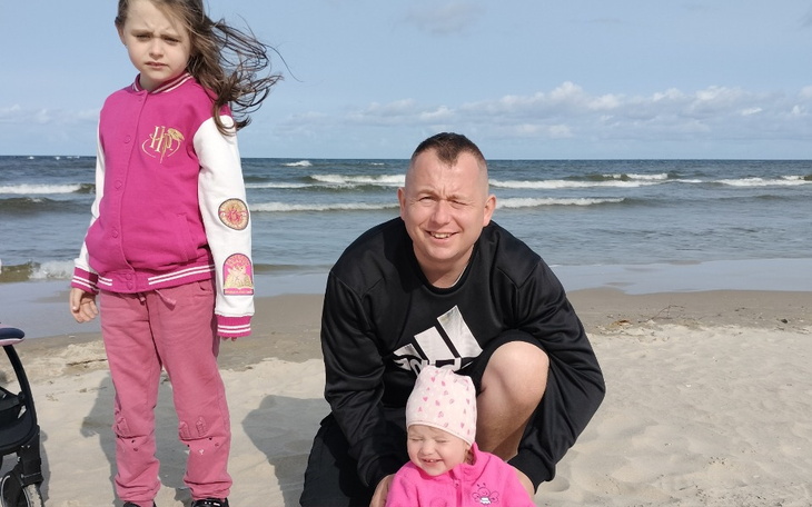 Rodzina na plaży, dzieci w różowych kurtkach, uśmiechnięty tata.