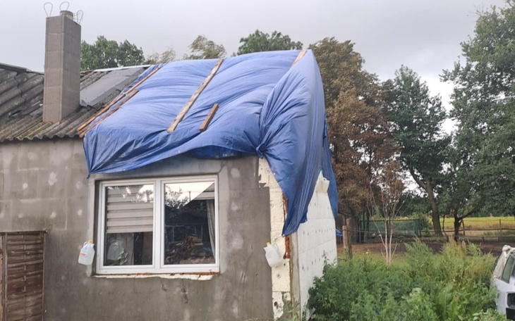 Dom z uszkodzoną elewacją i niebieską folią.