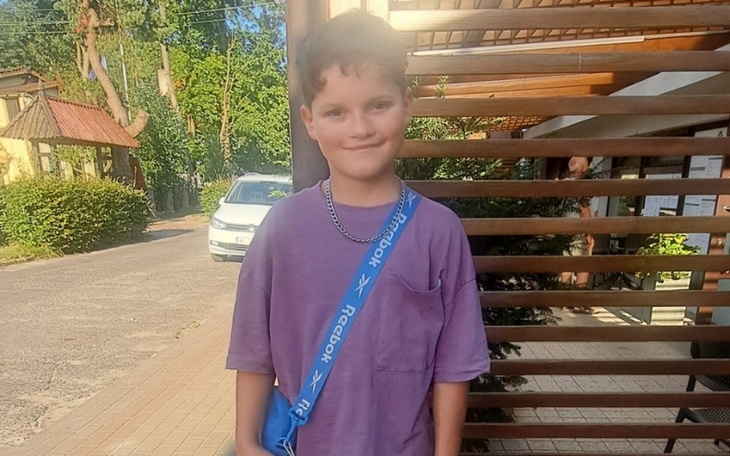 Chłopiec w fioletowej koszulce z torbą na ramieniu.