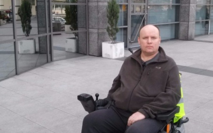 Mężczyzna na wózku inwalidzkim przed budynkiem.