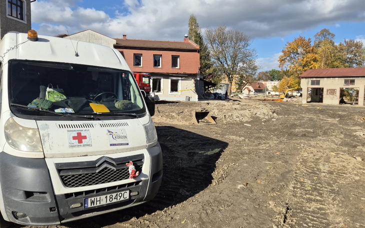 Samochód ratunkowy na placu budowy, w tle zniszczone budynki.