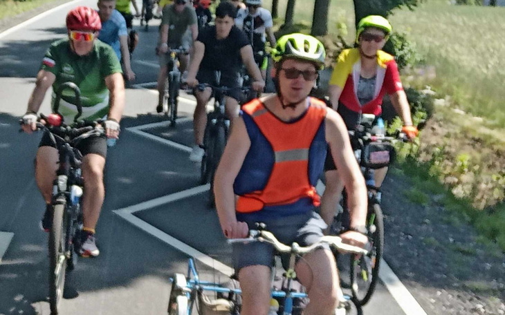 Grupa rowerzystów na drodze, w słoneczny dzień.
