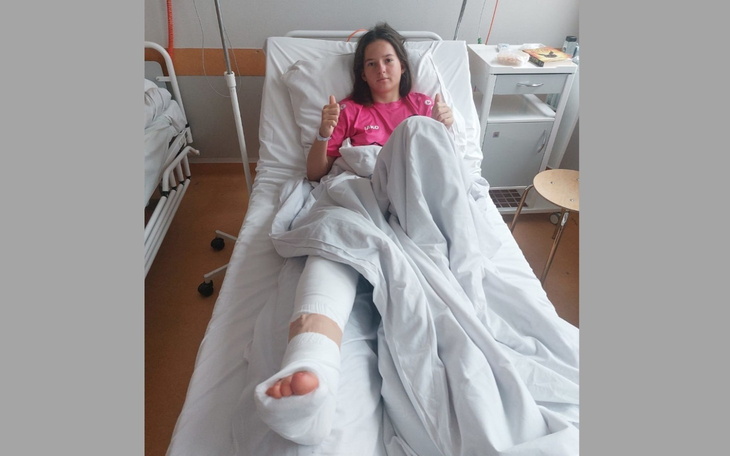 Młoda kobieta w szpitalnym łóżku, pokazująca kciuk w górę.