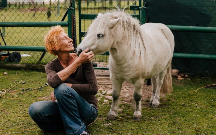 Kobieta przytulająca małego białego konika na łące.
