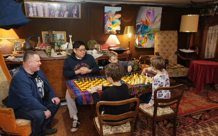 Grupa dzieci grających w szachy w przytulnym pomieszczeniu.